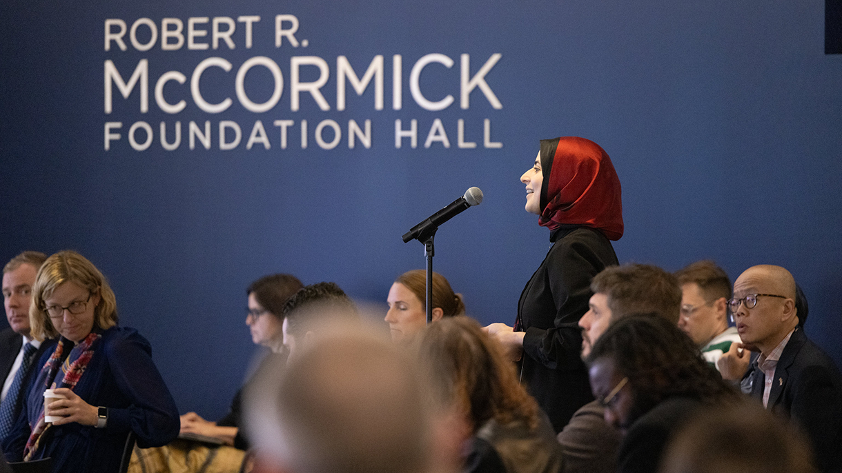 A woman stands at a microphone stand and asks a question at a Council event.