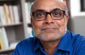 Prabhu Pingali is pictured from the shoulders up wearing a blue button-down shirt and smiling into the camera as he sits in a library.