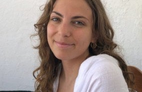Brita is pictured from the shoulders up wearing a long sleeved, white shirt, and is smiling into the camera.