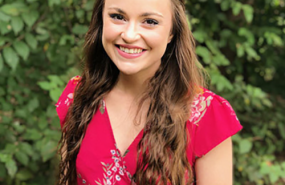 Mary Belle Zook smiles into the camera, pictured from the shoulders up wearing a pink floral shirt.