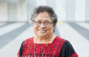 Myrna Cunningham smiles into the camera, pictured from the shoulders up wearing a red and black patterned shirt.