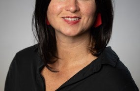 Sarah Evanega is pictured from the shoulders up wearing a black shirt, and is smiling into the camera.