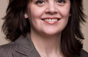 Jennifer Goldston is pictured from the shoulders up wearing a gray blazer and smiling into the camera.
