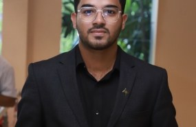 Abdullah Al Maruf is pictured from the waist up, looking into the camera, wearing a black suit jacket over a black button-up shirt.