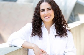 Rachel Abrams in a white professional button down shirt is smiling looking into the camera outside at Millennium Park