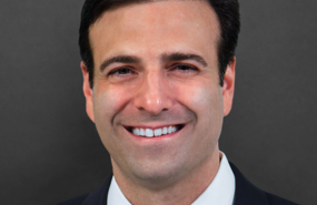 Heath Tarbert smiling with dark brown hair, red tie and jacket in front of grey background