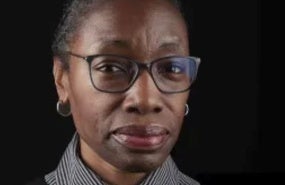 portrait of Comfort Ero wearing a grey shirt, black sweater vest, and glasses