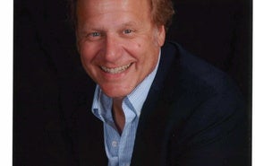 Headshot of Doug Scott wearing blue shirt and black jacket in front of black background