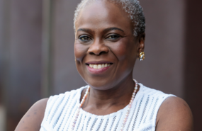 Headshot of Dr. Olopade smiling, wearing a white shirt, standing in front of grey background