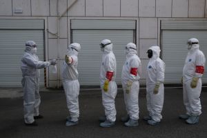 Volunteers in protective suits line up to be disinfected
