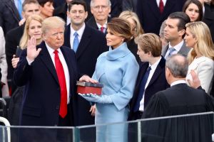 With right hand raised, Donald Trump looks at John Roberts with his back to the camera, as Melania Trump and others watch.