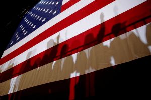  Shadows cast from a crowd of people in front of an American flag.