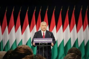 Viktor Orbán speaking at a podium in front of flags.