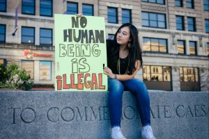 A young woman in Delaware holds a sign saying, "No human being is illegal"