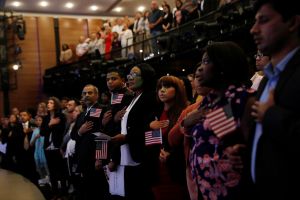 New citizens stand, while holding small American flags, during the National Anthem at a U.S. Citizenship and Immigration Services actualization ceremony.