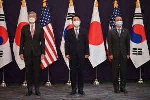 Sung Kim, Noh Kyu-duk, and Takehiro Funakoshi standing in front of flags on flag poles