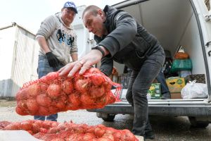 Two people holding big bag of onions, collecting humanitarian aid (water, food, hygiene products) for people evacuated from Donetsk and Lugansk People's Republics