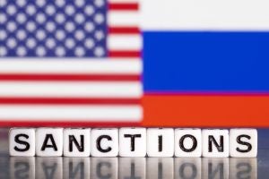 "Sanctions" on board game letters in front of Russian and American flag 