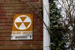 Fallout shelter sign on brick wall next to trees.