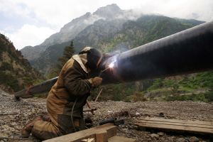 A welder works on a pipe with mountains in the background
