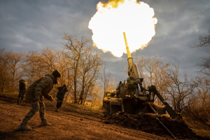 a cannon fires with flames and soldiers stand in the foreground, bare trees in the background in Ukraine.