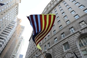 American flag with Ukraine flag colors in the white spots, blowing in the wind seen from below with skyscrapers behind.