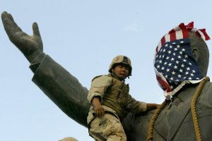 A Marine covers the face of a statue of Iraqi President Saddam Hussein with a US flag