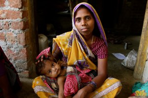 Shyamkali sits cross legged and holds her young daughter.