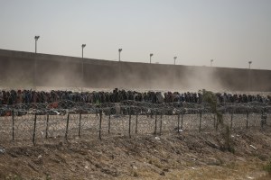 Migrants line-up between a barbed-wire barrier and the border fence at the US-Mexico border