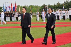 Kishida, right, and Yoon Suk Yeol, left, walk on a red carpet on green grass before troops.