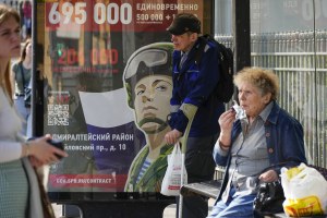 People wait a bus at a bus stop with an army recruiting billboard calling for a contract for service in the Russian armed forces