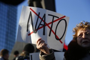 a woman holds a sign with NATO crossed out