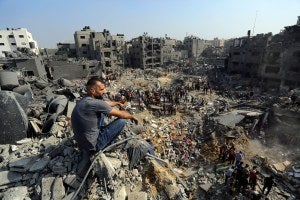 A man sits on the rubble as others wander among the debris of buildings that were targeted by Israeli airstrikes in Jabaliya refugee camp