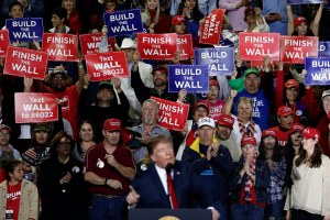 People hold signs that say finish the wall as Donald Trump speaks at a rally