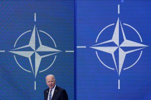 US President Joe Biden stands in front of the NATO logo