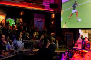 People sit around a bar, watching soccer on a TV