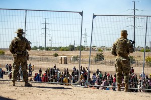 Migrants wait in line adjacent to the border fence under the watch of the Texas National Guard 