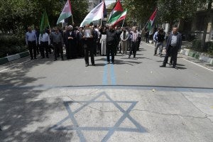 Protesters carry Iranian and Palestinian flags, while an image of the Israeli flag is painted on the ground