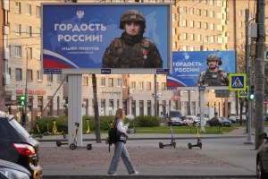 A woman walks past advertising billboards which show Russian soldiers