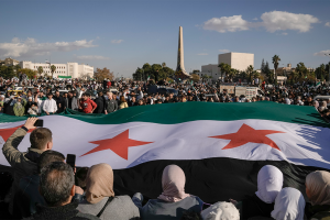 Syrians display a giant "revolutionary" Syrian flag during a celebratory demonstration following the first Friday prayers since Bashar Assad's ouster, in Damascus' central square, Syria, on Friday, Dec. 13, 2024.