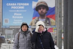 Women walk past a billboard with a portrait of a Russian soldier awarded for action in Ukraine and the words Glory to the heroes of Russia