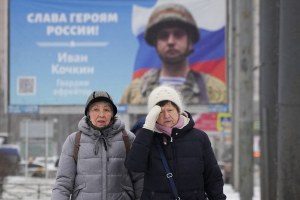 Women walk past a billboard with a portrait of a Russian soldier awarded for action in Ukraine and the words Glory to the heroes of Russia