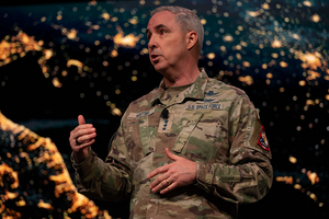 General Stephen N. Whiting speaks in front of a screen showing a close-up photo of Earth from space.