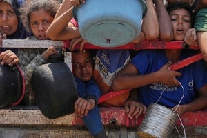 Palestinians push up against a fence waiting for food at a community kitchen in Gaza City on July 26, 2025.