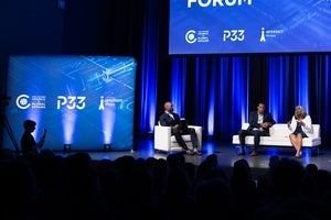 Three people sit in chairs on a stage in front of a crowd