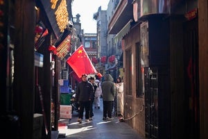People walk past a Chinese flag in a Beijing commercial area on February 3, 2025. 