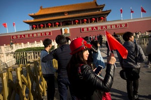 A woman holds a Chinese flag as she poses for a photo near Tiananmen Gate