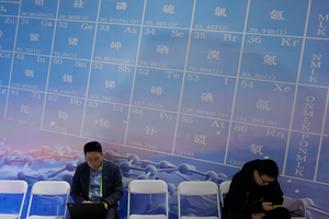 Men sit near a periodic table showing minerals at the China International Supply Chain Expo in Beijing on November 27, 2024.