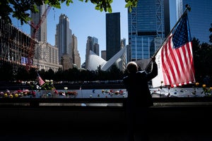 a man holds an American flag near the National September 11 Memorial and Museum