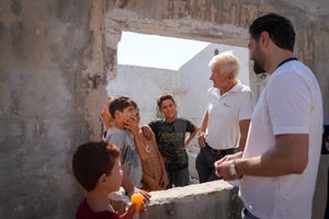 Jan Egeland standing and speaking with a man and children in Idlib, Syria.